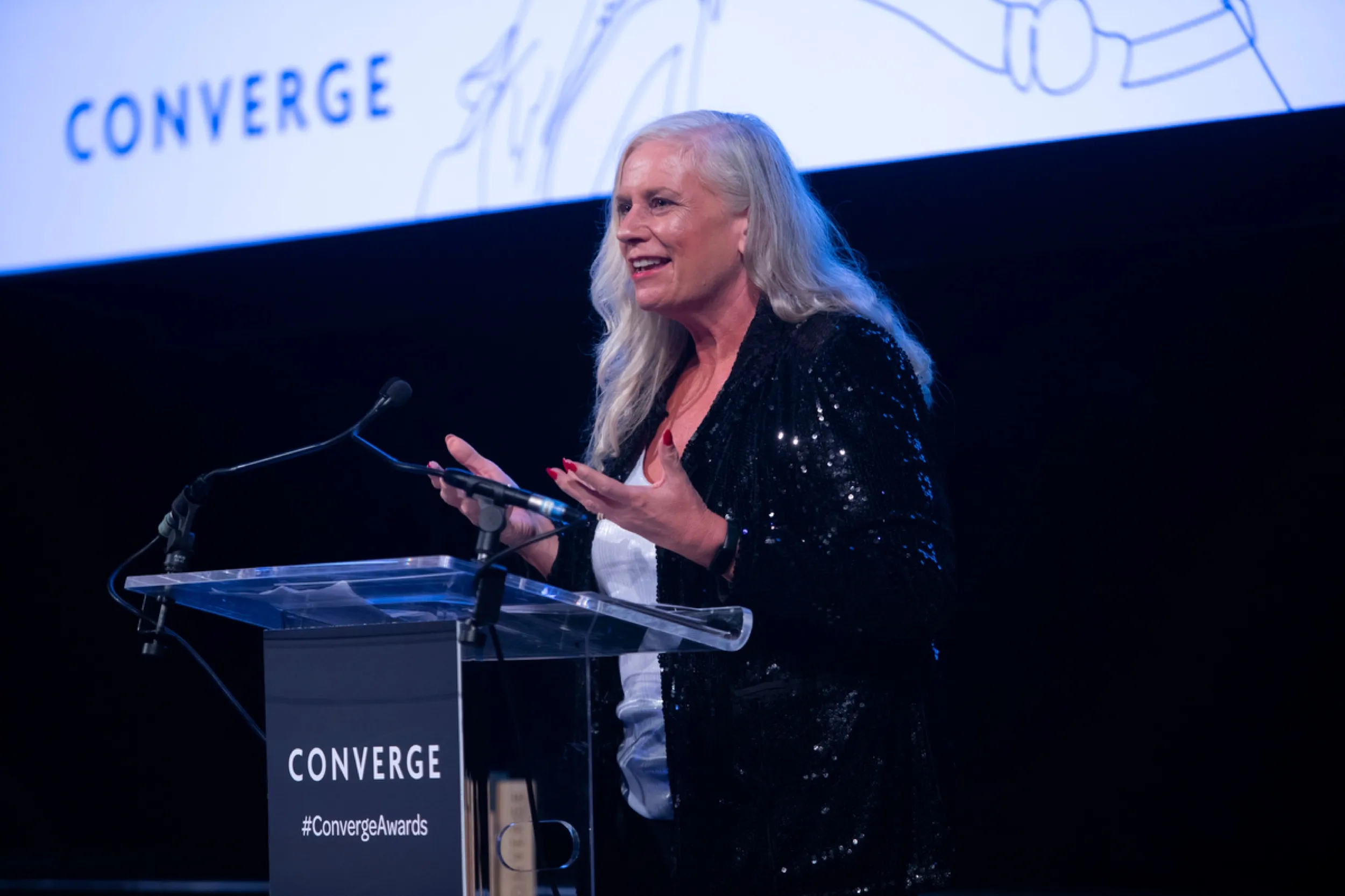 Alison at the podium of the Converge Awards, mid-speech in a sequinned jacket.