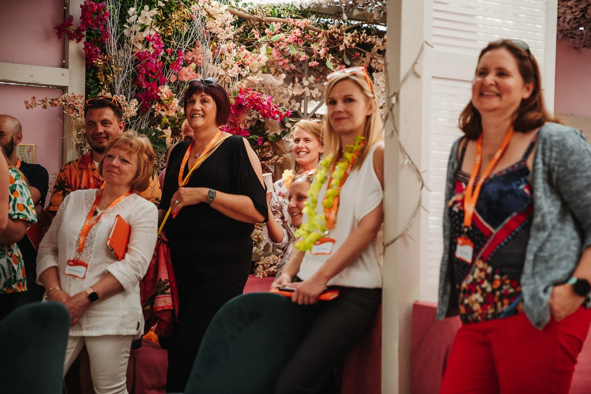 Delegates in lanyards standing together and smiling at a team event, in a room dressed with pink and white flowers.