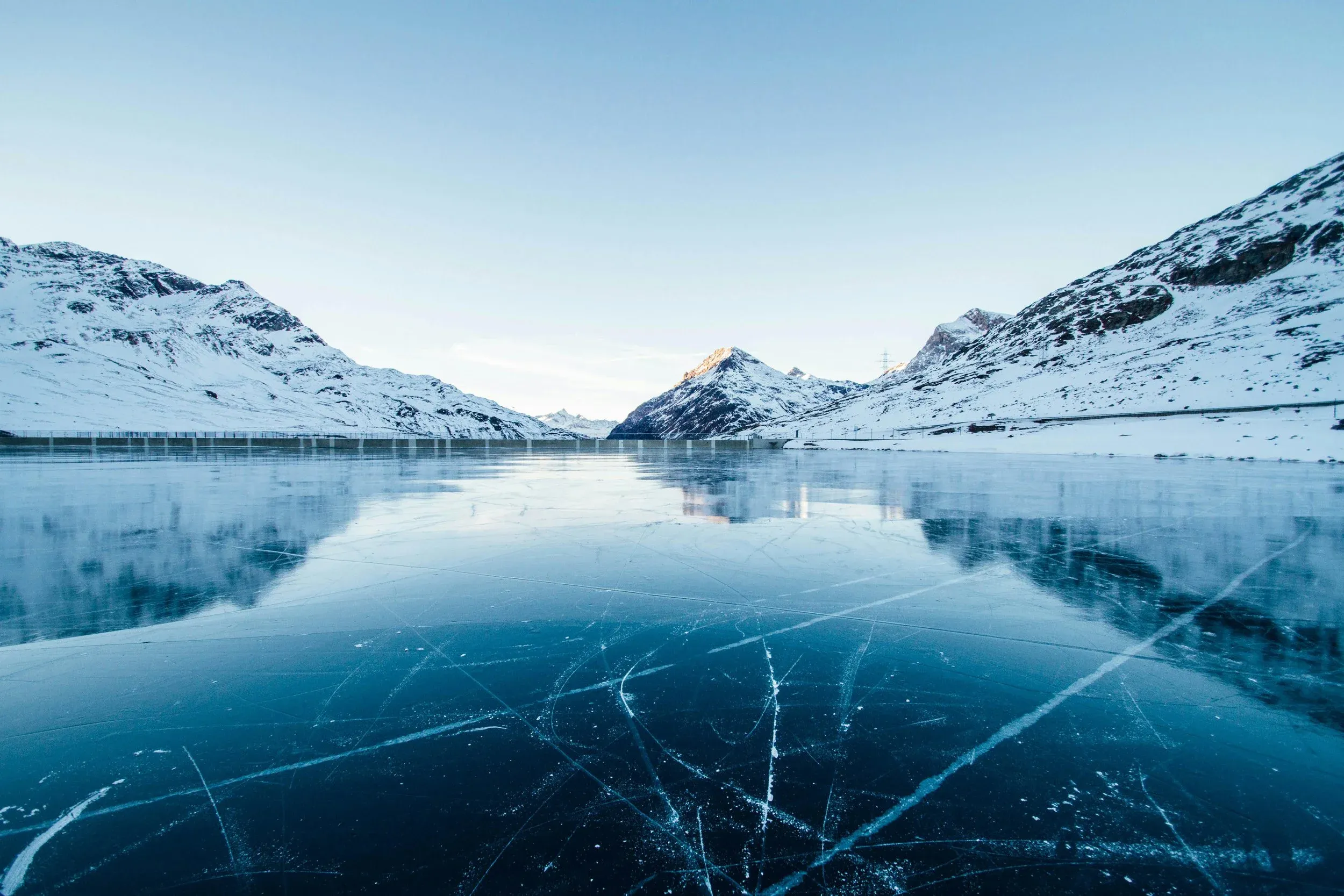 A frozen lake with long cracks running across the ice, ringed by snow-covered mountains.