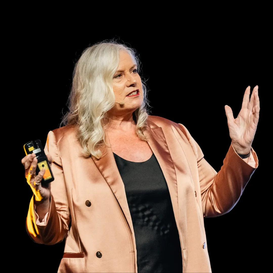 Dr Alison Edgar MBE against a black background, one hand raised and a clicker in the other, mid-sentence.