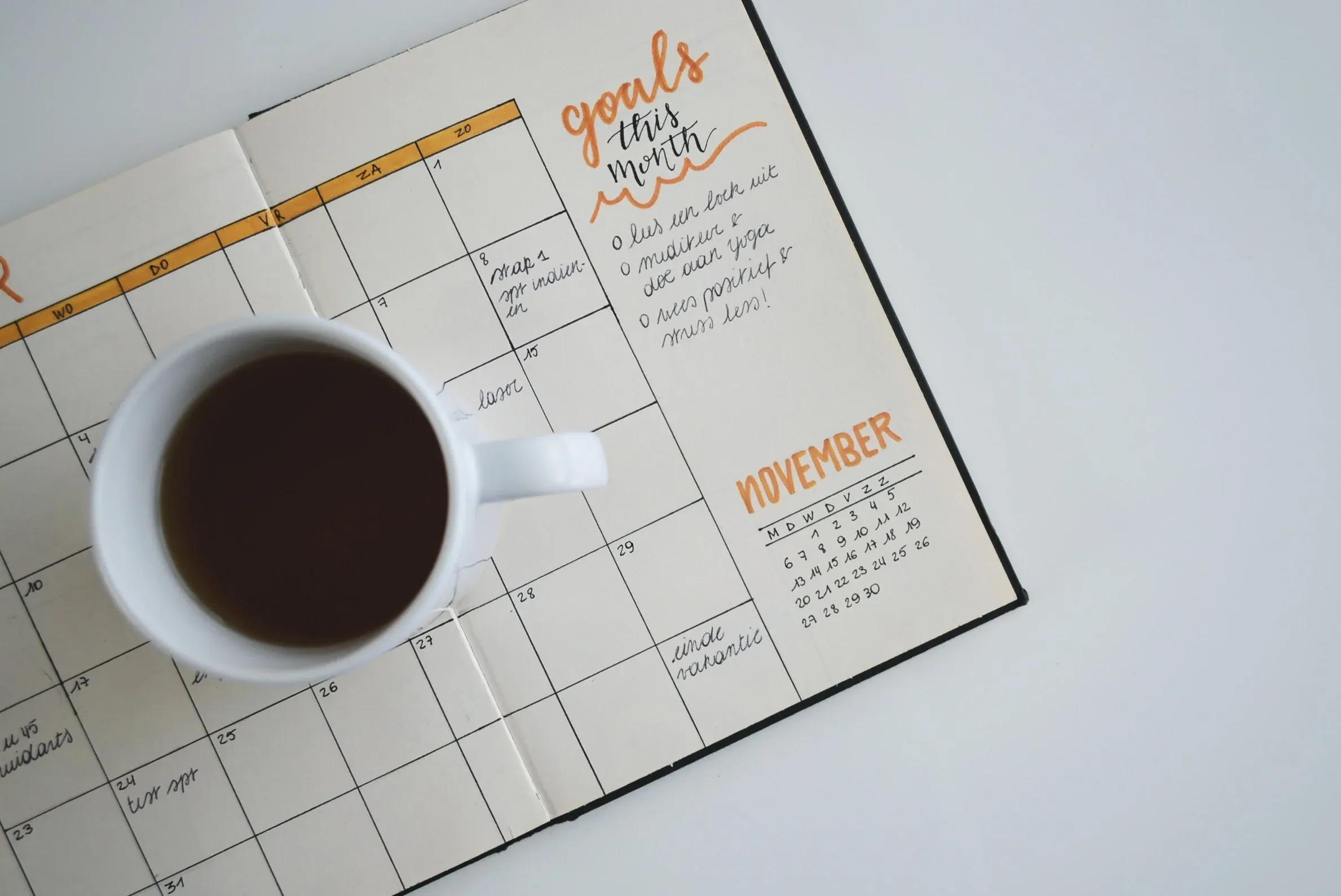 An open planner showing a handwritten 'goals this month' list for November, a cup of coffee resting on the facing page.