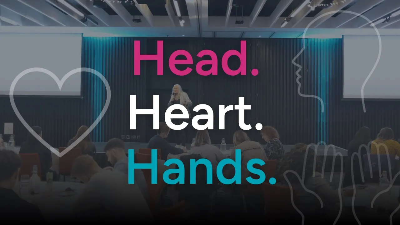 Head. Heart. Hands. in large pink, white and teal type over a photo of Dr Alison Edgar MBE speaking on stage to a room of delegates at round tables, with line drawings of a heart, a head in profile and a raised hand.